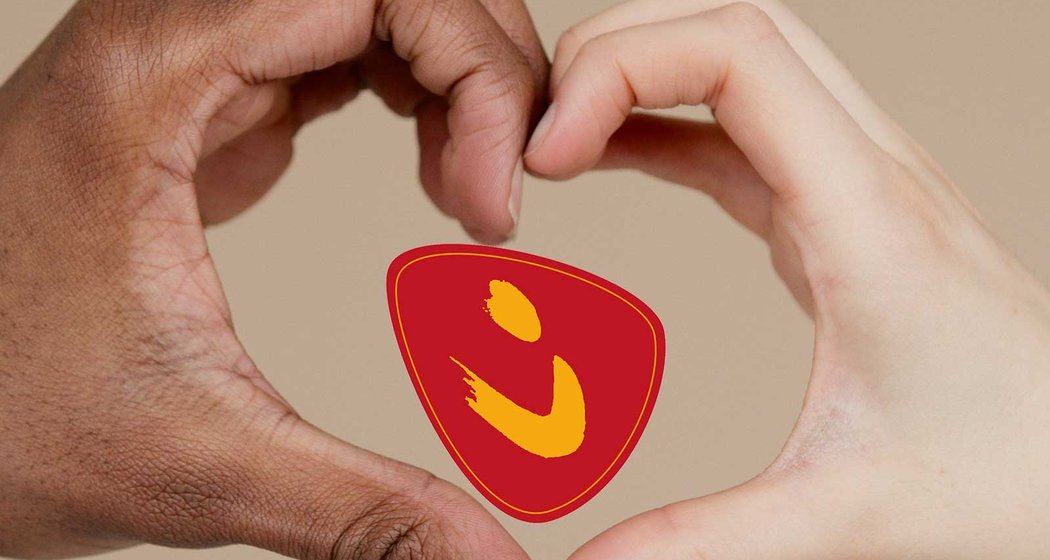Zwei Hände, eine dunkelhäutige und eine hellhäutige, bilden zusammen eine Herzform. Im Inneren des Herzens befindet sich ein rotes Logo mit einem gelben abstrakten Muster auf beigem Hintergrund.