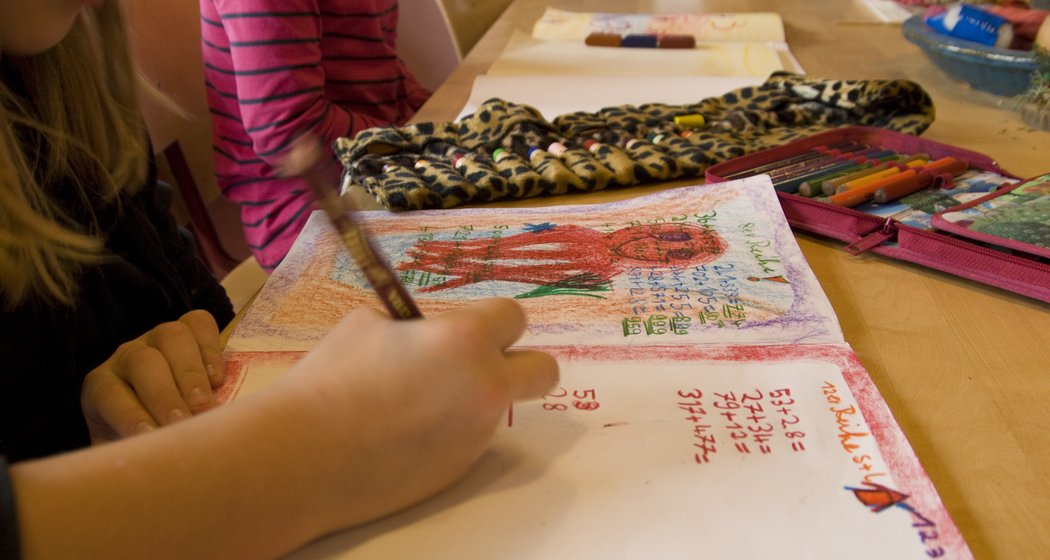 Ein Kind zeichnet und malt in einem Skizzenbuch an einem Tisch, in dessen Nähe sich Buntstifte und Malutensilien befinden. Andere Kinder sitzen ebenfalls am Tisch und beschäftigen sich mit ihren eigenen kreativen Projekten.
